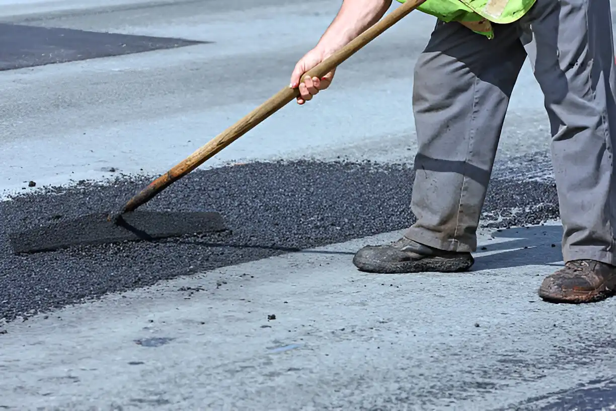 Man raking pothole repair compound and smoothing it
